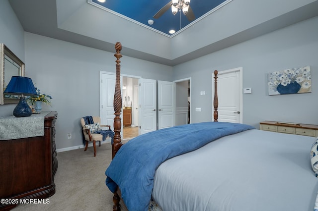 bedroom with light carpet, baseboards, connected bathroom, ceiling fan, and a tray ceiling