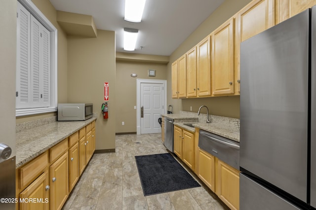 kitchen featuring appliances with stainless steel finishes, light brown cabinetry, a sink, and light stone countertops