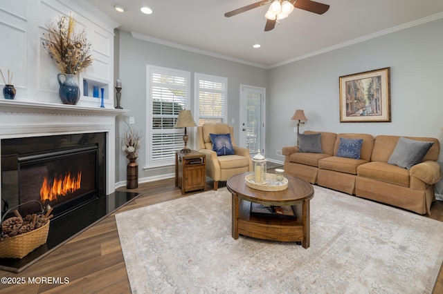 living area with baseboards, a glass covered fireplace, wood finished floors, crown molding, and recessed lighting