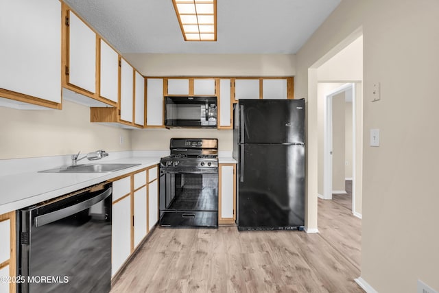 kitchen with baseboards, light wood-style flooring, light countertops, black appliances, and a sink