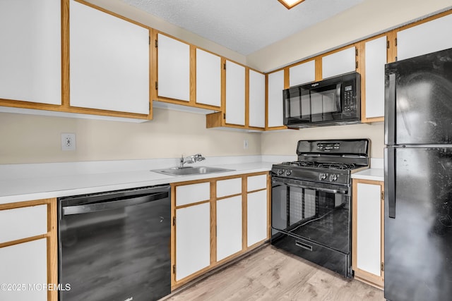 kitchen featuring light countertops, a sink, light wood-style flooring, and black appliances