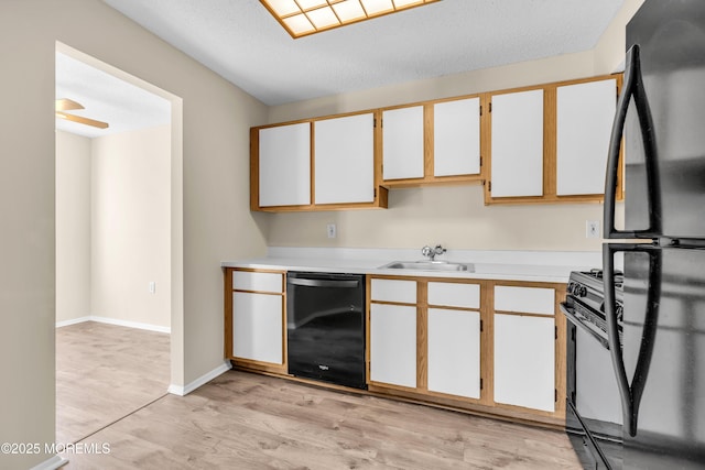 kitchen featuring light wood finished floors, light countertops, a sink, black appliances, and baseboards