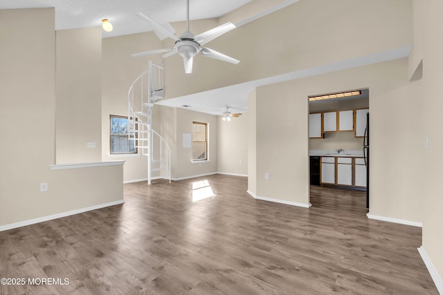 unfurnished living room with stairs, wood finished floors, a ceiling fan, and baseboards