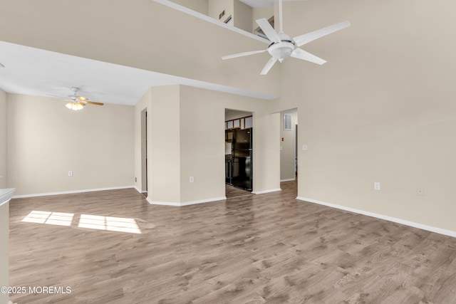 empty room featuring a ceiling fan, a high ceiling, baseboards, and wood finished floors