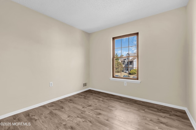 unfurnished room with baseboards, a textured ceiling, visible vents, and wood finished floors