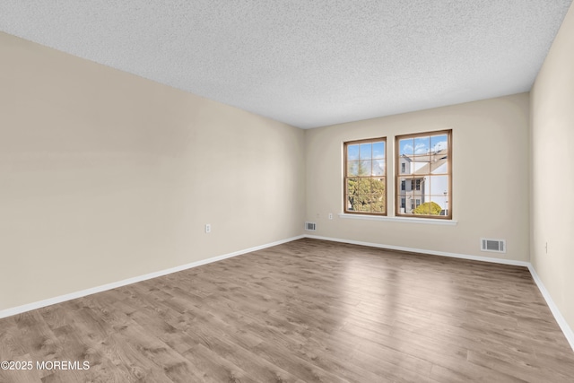 spare room featuring wood finished floors, visible vents, and baseboards