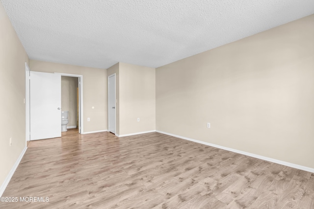 unfurnished room with light wood-type flooring, baseboards, and a textured ceiling