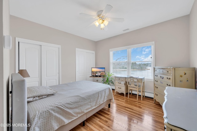 bedroom featuring visible vents, multiple closets, light wood-style flooring, a ceiling fan, and baseboard heating