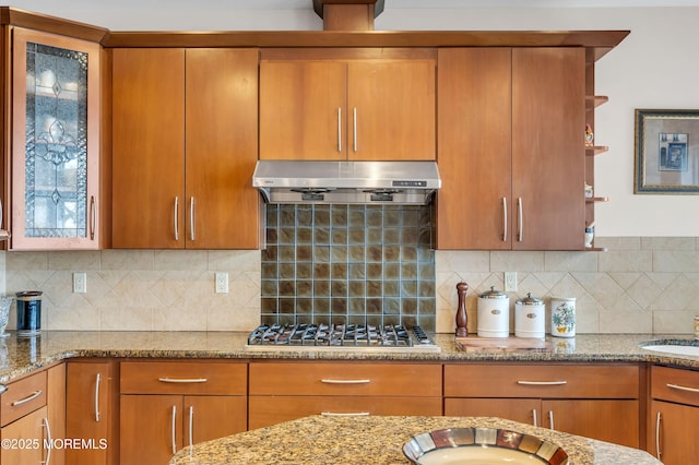 kitchen featuring under cabinet range hood, open shelves, tasteful backsplash, light stone countertops, and stainless steel gas cooktop