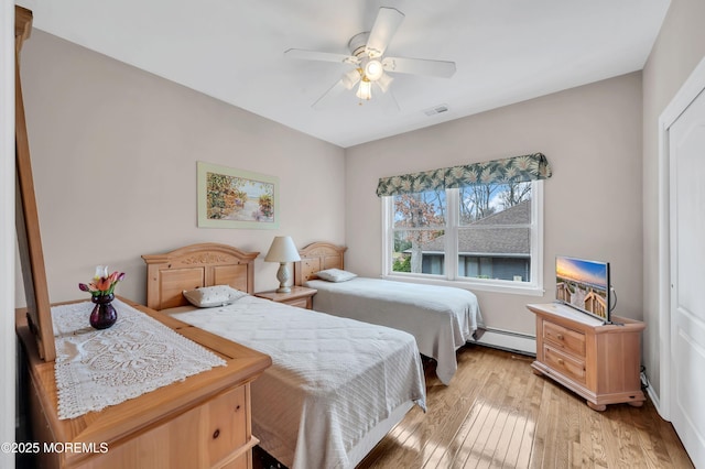bedroom featuring light wood finished floors, visible vents, a ceiling fan, and a baseboard radiator