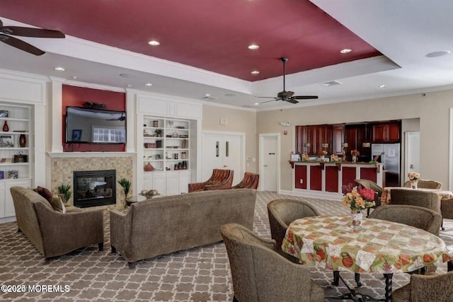 living room with a fireplace, built in features, a raised ceiling, and crown molding