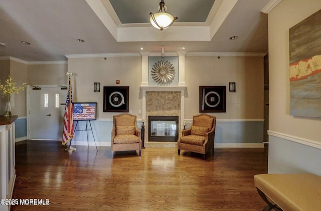 sitting room with a tiled fireplace, a tray ceiling, wood finished floors, and ornamental molding