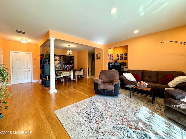 living area with decorative columns, visible vents, baseboards, wood finished floors, and a notable chandelier