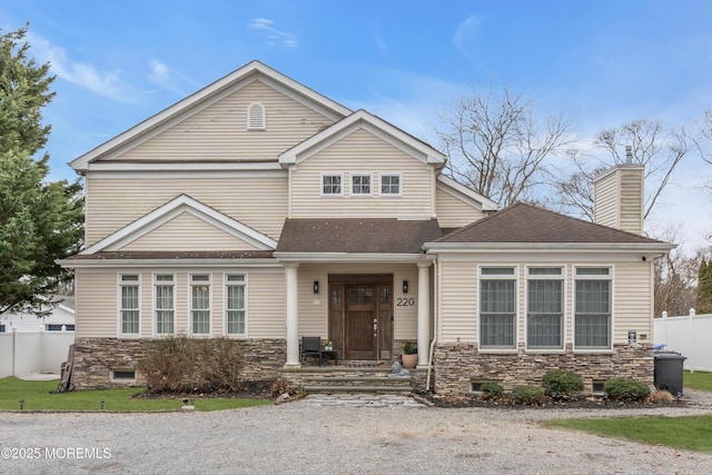 view of front of house with stone siding, a shingled roof, a chimney, and fence