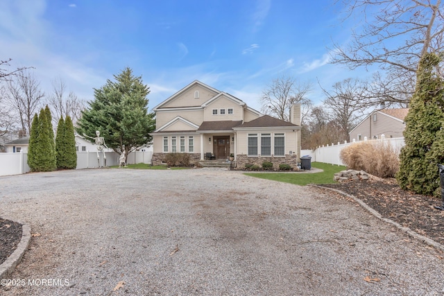 view of front facade featuring stone siding, fence, a chimney, and gravel driveway