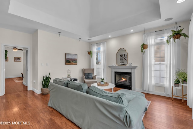 living room featuring recessed lighting, wood-type flooring, a glass covered fireplace, and baseboards