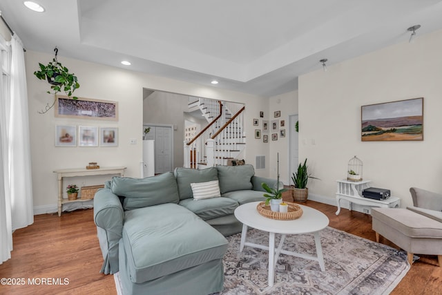 living area featuring light wood-type flooring, stairway, and a tray ceiling