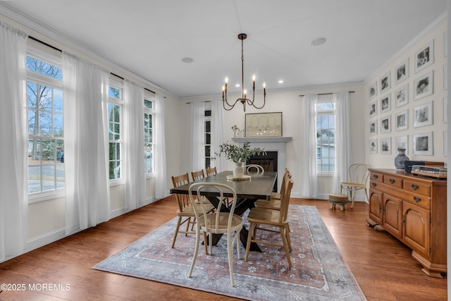 dining area featuring an inviting chandelier, a glass covered fireplace, crown molding, and wood finished floors