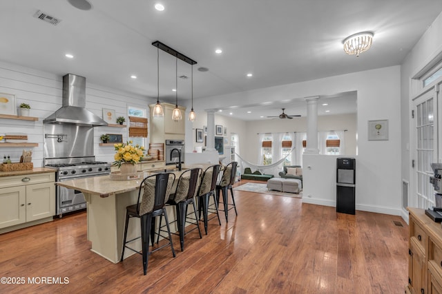 kitchen featuring decorative columns, open shelves, stainless steel appliances, visible vents, and wall chimney range hood