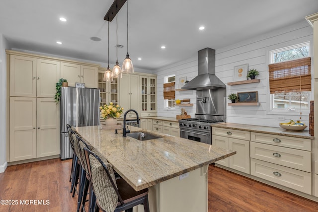 kitchen featuring appliances with stainless steel finishes, wood finished floors, cream cabinets, ventilation hood, and a sink