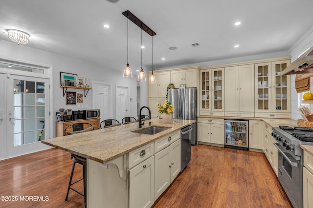 kitchen with wine cooler, cream cabinets, a breakfast bar, a sink, and appliances with stainless steel finishes