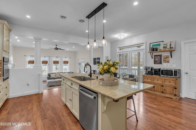 kitchen with decorative columns, appliances with stainless steel finishes, a breakfast bar, wood finished floors, and a sink