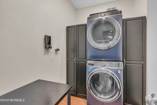 clothes washing area with cabinet space, light wood-style flooring, and stacked washer / dryer