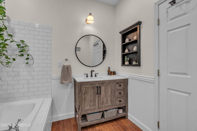 full bathroom with tiled bath, wainscoting, vanity, and wood finished floors