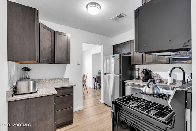 kitchen with stainless steel appliances, visible vents, dark brown cabinetry, and light wood-style flooring