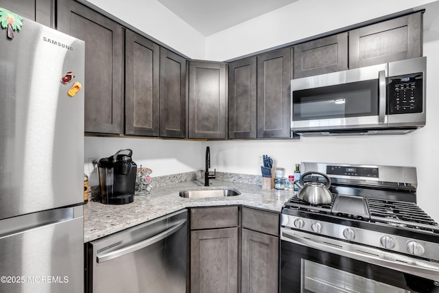 kitchen featuring stainless steel appliances, a sink, light stone counters, and dark brown cabinetry