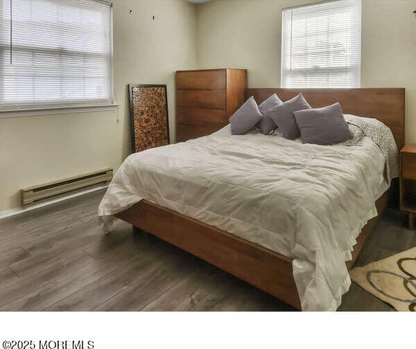 bedroom with a baseboard heating unit, multiple windows, and wood finished floors