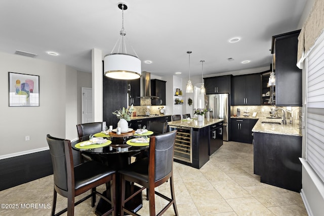 kitchen with stainless steel appliances, a kitchen island, a sink, dark cabinetry, and wall chimney exhaust hood