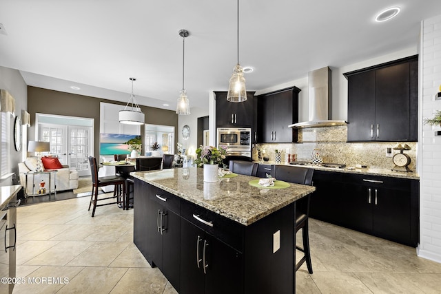 kitchen with wall chimney range hood, stainless steel appliances, dark cabinets, and a center island