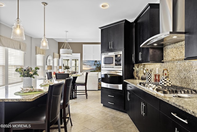 kitchen with wall chimney range hood, tasteful backsplash, appliances with stainless steel finishes, and dark cabinets