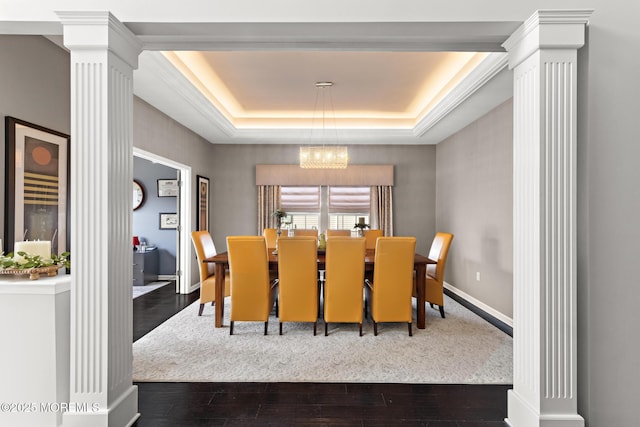 dining room with baseboards, decorative columns, a tray ceiling, and wood finished floors