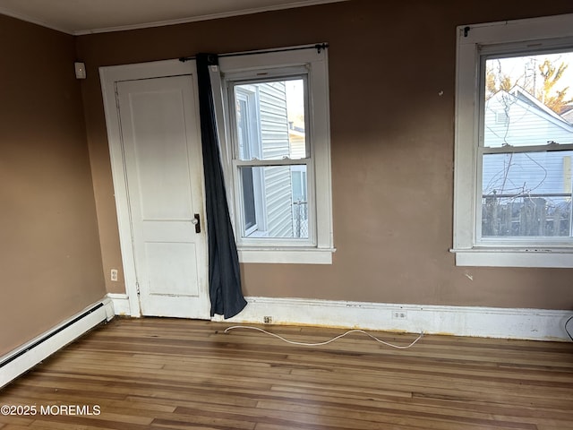 spare room with a baseboard heating unit, ornamental molding, wood finished floors, and baseboards