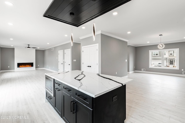 kitchen featuring crown molding, a large fireplace, open floor plan, light wood-type flooring, and dark cabinets