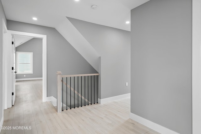 hall featuring baseboards, an upstairs landing, lofted ceiling, and light wood finished floors