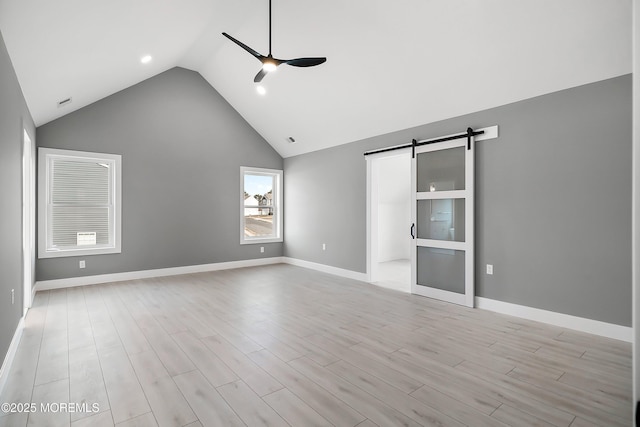 unfurnished bedroom featuring lofted ceiling, baseboards, light wood-type flooring, and a barn door