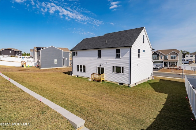 back of house featuring fence, a residential view, roof with shingles, and a lawn