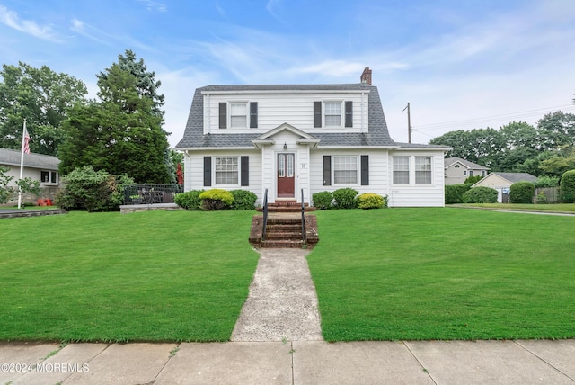 colonial inspired home featuring a front yard, roof with shingles, and a chimney