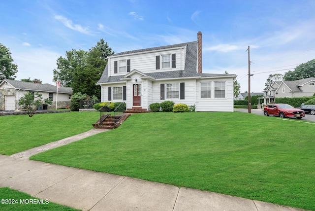 dutch colonial featuring a shingled roof, a chimney, and a front yard