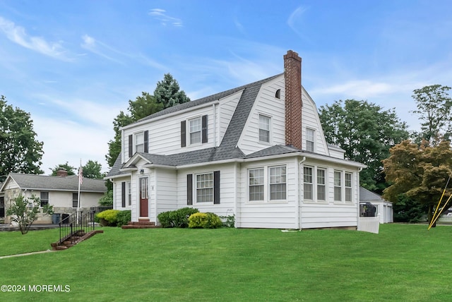 colonial inspired home with a shingled roof, a chimney, a front lawn, and a gambrel roof