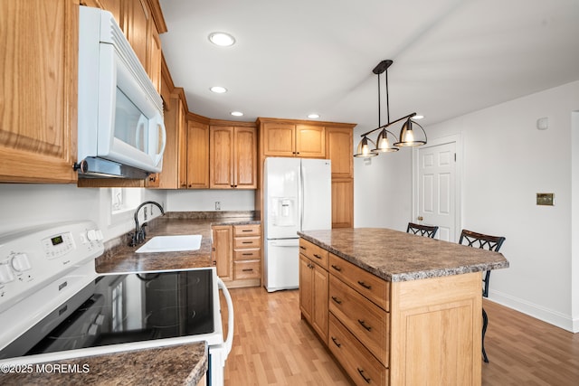 kitchen with light wood-type flooring, white appliances, dark countertops, and a sink