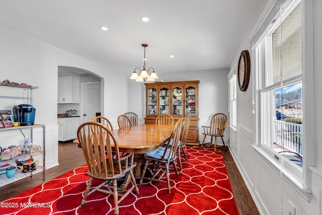 dining space with arched walkways, a wainscoted wall, a notable chandelier, recessed lighting, and dark wood-type flooring