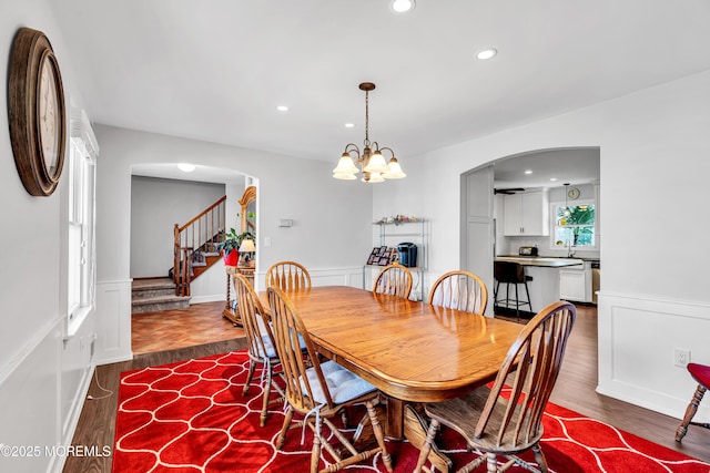 dining space featuring dark wood-style floors, arched walkways, wainscoting, and stairs