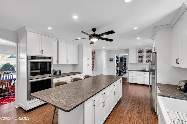 kitchen with dark wood finished floors, tasteful backsplash, white cabinets, a kitchen island, and a kitchen bar