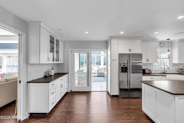 kitchen featuring dark countertops, glass insert cabinets, dark wood-style flooring, stainless steel refrigerator with ice dispenser, and a sink