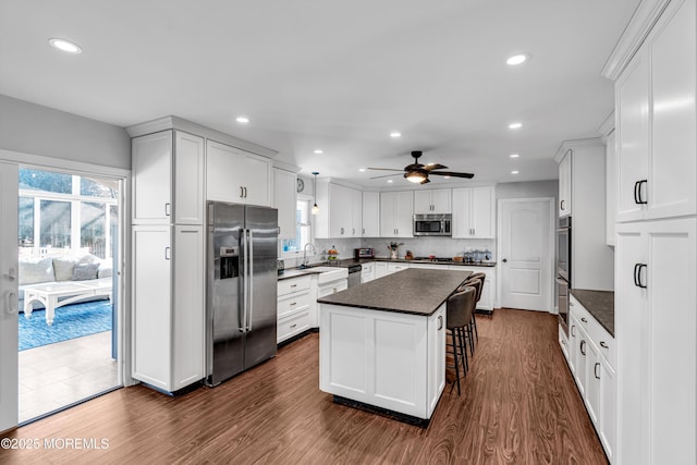 kitchen featuring white cabinets, dark countertops, dark wood-style flooring, a center island, and stainless steel appliances