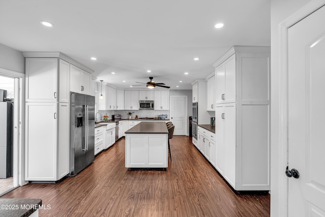 kitchen with dark countertops, a kitchen island, dark wood-type flooring, stainless steel appliances, and white cabinetry